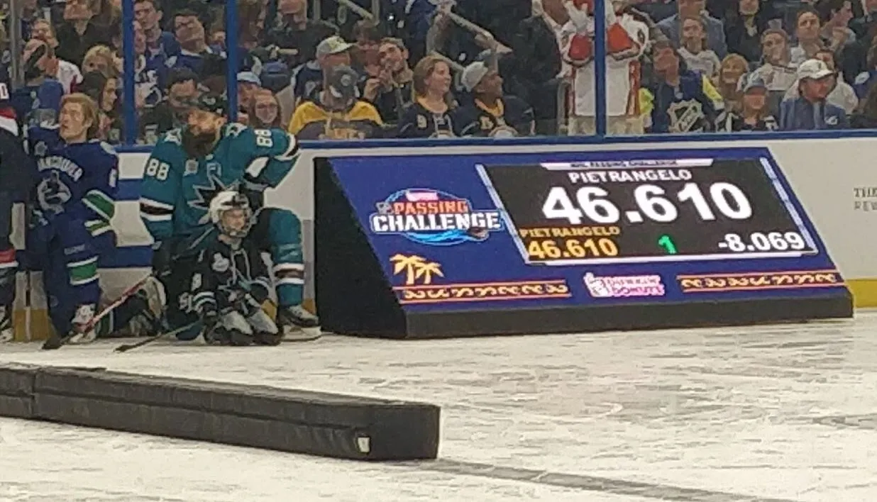 A hockey player sitting on the ice next to a scoreboard.